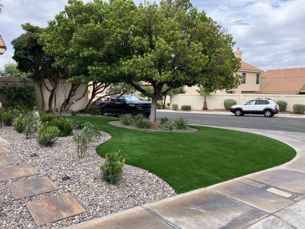a tree in front of a house with a circle of artificial turf around it with a car behind it