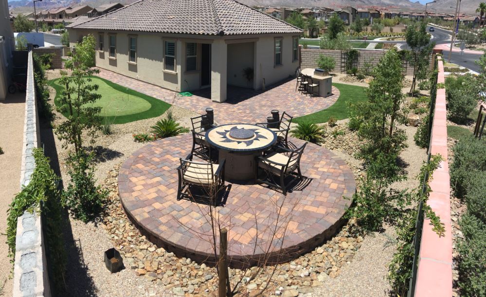 Aerial view of Las Vegas backyard featuring a circular paver patio with outdoor dining set, synthetic turf putting green, desert gravel landscaping, and young shade trees by Southwest Greens of Nevada