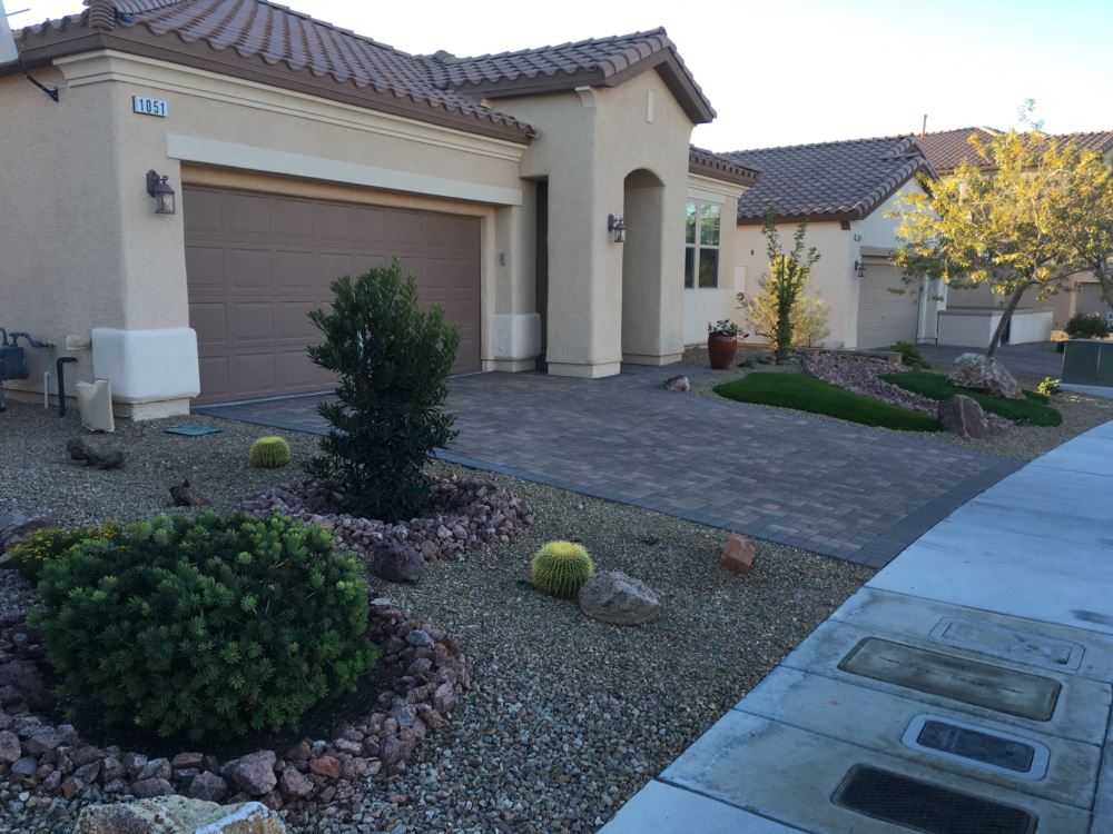 Desert-landscaped front yard with paver driveway, barrel cacti, native shrubs, and synthetic turf island accent at a Henderson Nevada home by Southwest Greens of Nevada