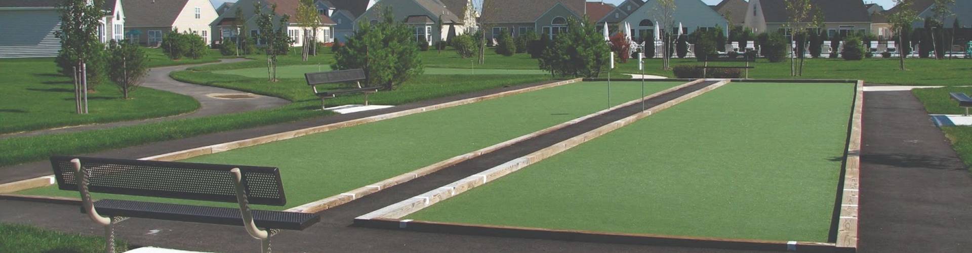 Artificial turf installation on two bocce ball courts with wood borders and spectator benches in a residential community with a putting green in the background