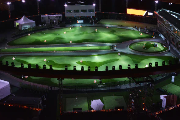 Large-scale artificial turf installation at a nighttime golf entertainment venue, featuring illuminated synthetic putting greens and custom-designed practice areas.