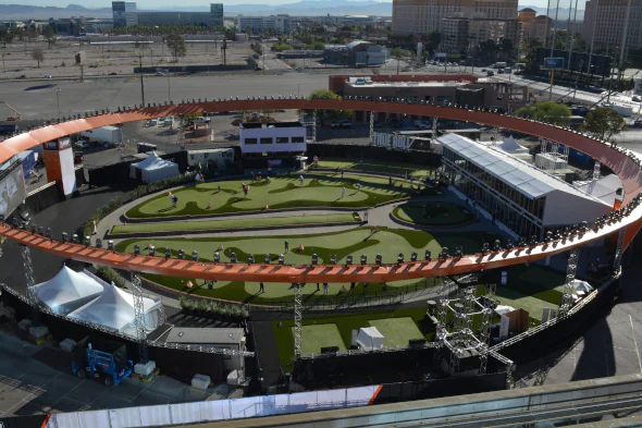 Aerial view of large-scale artificial turf installation at an outdoor golf entertainment venue, featuring contoured greens, target zones, and professional lighting within a custom event structure.